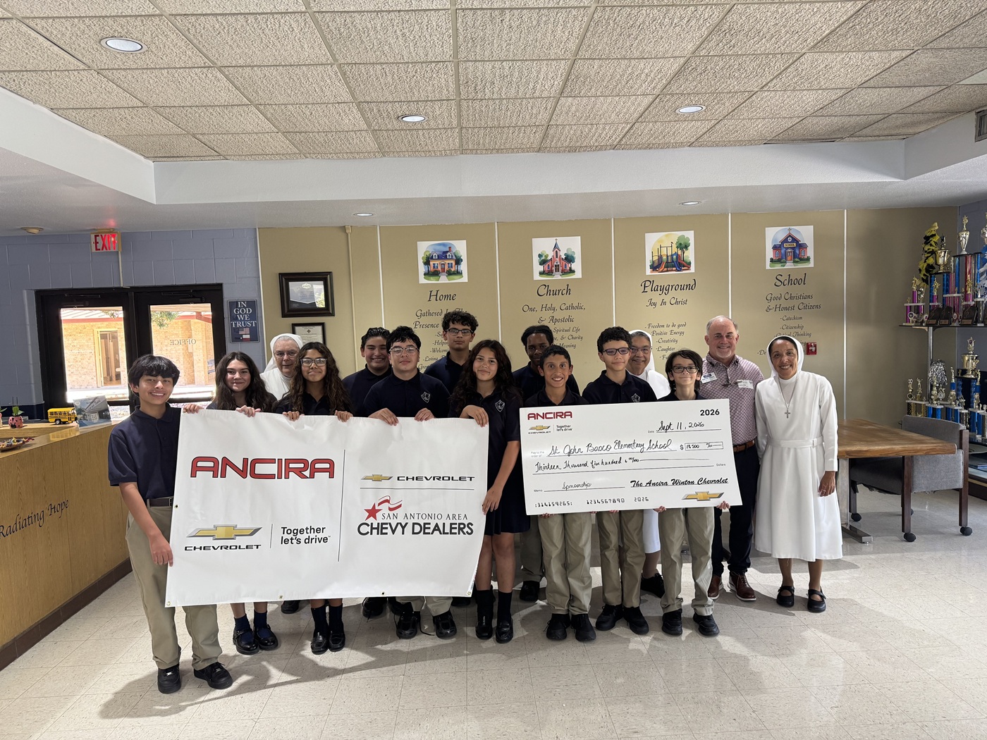 Darrell Dixon, the GM of Ancira Winton Chevy, presenting a check to help Little Flower Catholic School. One is $500 for their sports program, and the other is $13,000 for their operating fund.